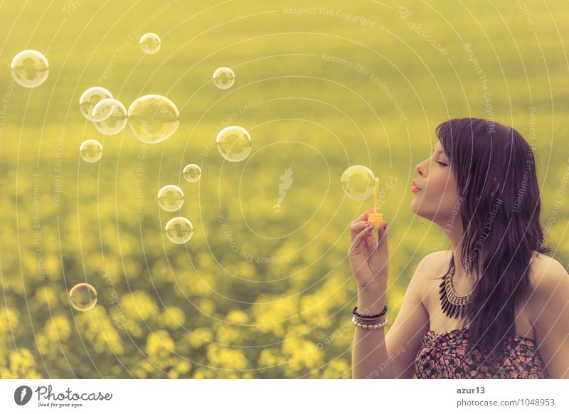 Schöne junge Frau pustet Seifenblasen im Sommer auf gelber Wiese aus Raps bis zum Horizont. Hübsches Mädchen mit Lebensfreude geniesst die Sonnenschein Pause und das Leben. Erholung und Energie tanken vom Zeit Stress in der Umwelt und Natur Idylle.