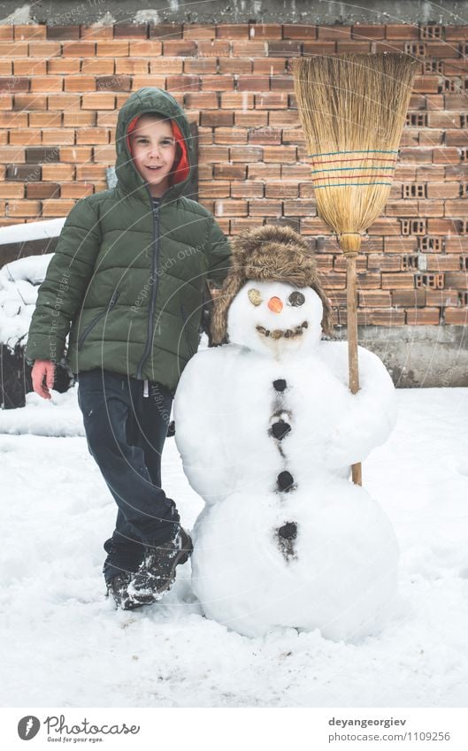 Schneemann und Kind im Hof Freude Glück Spielen Ferien & Urlaub & Reisen Winter Junge Frau Erwachsene Kindheit Natur Gebäude Hut Lächeln Fröhlichkeit weiß