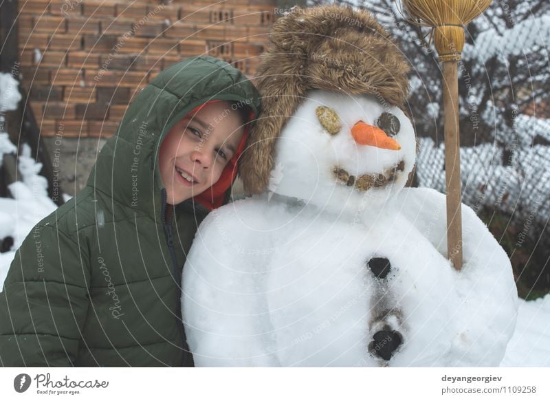 Schneemann und Kind im Hof Freude Glück Spielen Ferien & Urlaub & Reisen Winter Junge Frau Erwachsene Kindheit Natur Gebäude Hut Lächeln Fröhlichkeit weiß