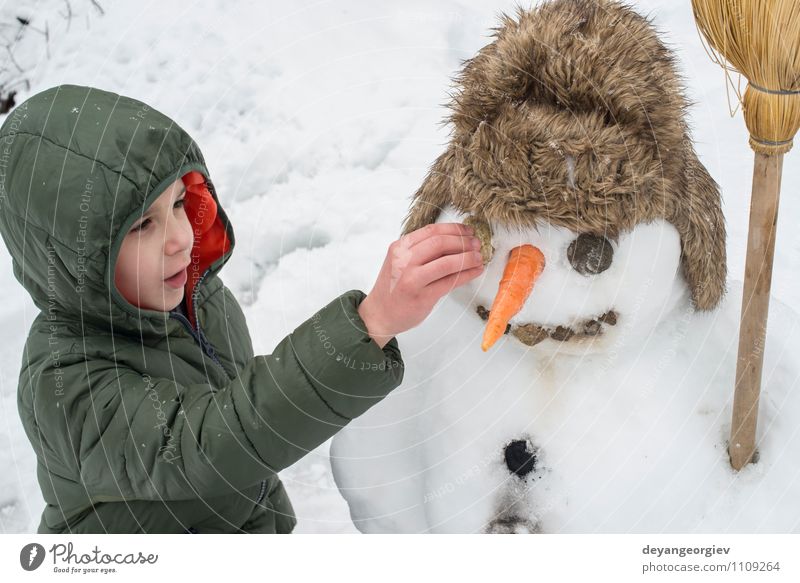 Schneemann und Kind im Hof Freude Glück Spielen Ferien & Urlaub & Reisen Winter Junge Frau Erwachsene Kindheit Natur Gebäude Hut Lächeln Fröhlichkeit weiß