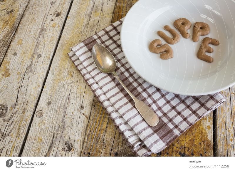 Die Buchstaben SUPPE in einem Suppenteller mit Löffel und Serviette auf einem rustikalen Holztisch Lebensmittel Eintopf Mittagessen Abendessen Büffet Brunch