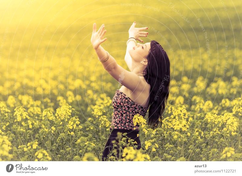 Schöne junge Frau im Sommer auf gelber Wiese aus Raps bis zum Horizont. Hübsches Mädchen mit Lebensfreude geniesst die Sonnenschein Pause und das Leben. Erholung und Energie tanken vom Zeit Stress in der Umwelt und Natur Idylle. Hände nach oben, Augen zu.