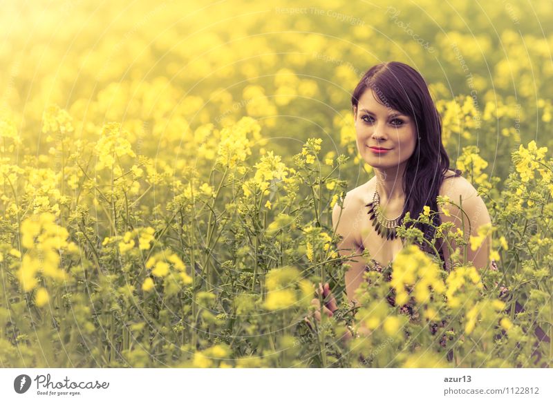 Glückliche Sommer Liebe Frau sitzt lächelnd im Rapsfeld. Attraktives junges Schönheit Mädchen, dass die warme, sonnige Sonne in der Natur genießt, nimmt sich Zeit, um Nachhaltigkeit, Besinnung und jugendliches Wohlbefinden zu spüren.