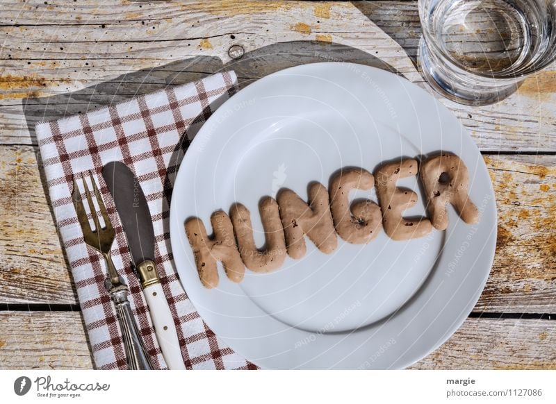 Die Buchstaben HUNGER auf einem Teller mit Messer und Gabel und Serviette und einem Glas Wasser Ernährung Diät Fasten Appetit & Hunger Getränk