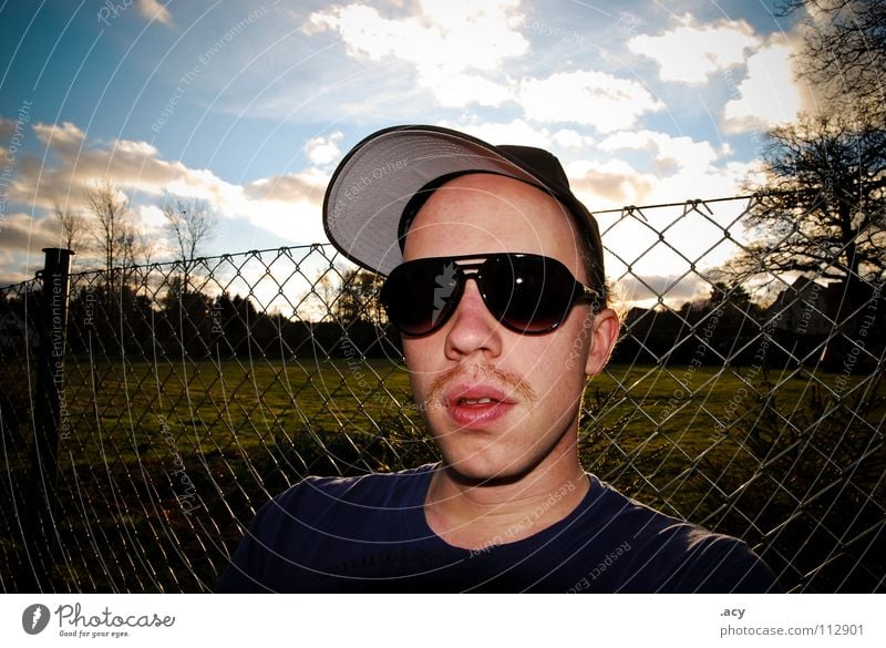 kalle chillt Oberlippenbart Bart Pornographie Brille Sonnenbrille Osten Maschendraht Maschendrahtzaun Zaun Wolken Porträt Baseballmütze Mann Jugendliche