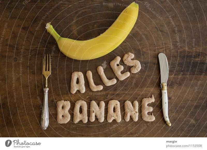 Die Buchstaben ALLES BANANE mit einer Banane und Messer und einer Gabel auf einem rustikalen Holztisch Lebensmittel Frucht Ernährung Frühstück Mittagessen