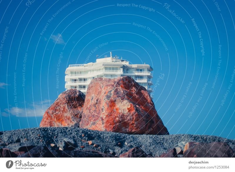 Felsenhotel? Ein Großer roter Felsen liegt am Strand vor einem  weißen Hotel. Blauer Himmel im Hintergrund. Haus am Strand von Burleigh Heads. Queensland. Australia