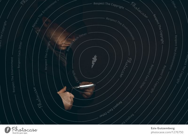 Mann prüft sein Rasiermesser in der Dunkelheit Stil Körperpflege Mensch maskulin Gesicht Hand Finger 1 30-45 Jahre Erwachsene Mantel Schal Hut Zopf Bart