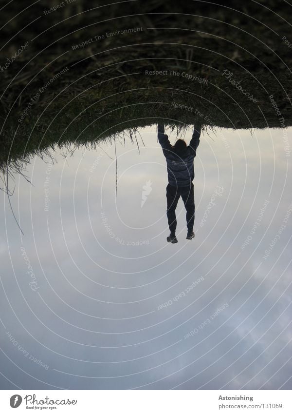 Cliffhanger Wiese Mann hängen Handstand verkehrt stehen festhalten schwarz gefährlich Bewegung Himmel Bodenbelag Kontrast Abend