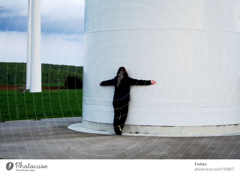 WindRiesen Frau Windkraftanlage Umarmen Elektrizität Feld Wiese Hügel Wolken Baum Wäldchen Beton weiß groß Macht Gras Koloss braun Jacke drücken festhalten Hand