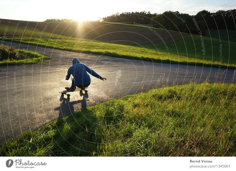 Rechtskurve abwärts schön Skateboarding Sonnenuntergang gelb grün Wiese Feld Asphalt Kurve Straße Freude spaßig Bewegung Kurvenlage Dynamik Mann Kapuzenpullover