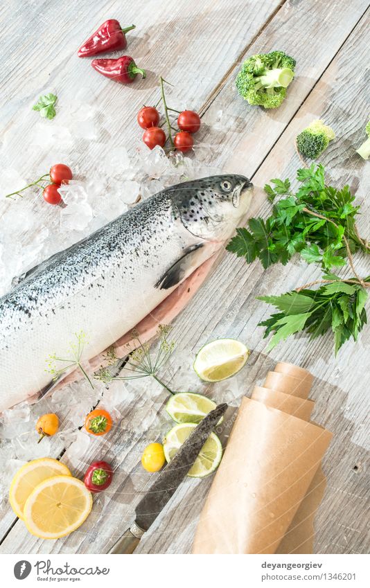 Rohe Lachsfische im Eis Meeresfrüchte Gemüse Abendessen Tisch Koch Papier frisch lecker rot weiß Fisch Lebensmittel roh Zitrone Backpapier Messer hölzern Tomate