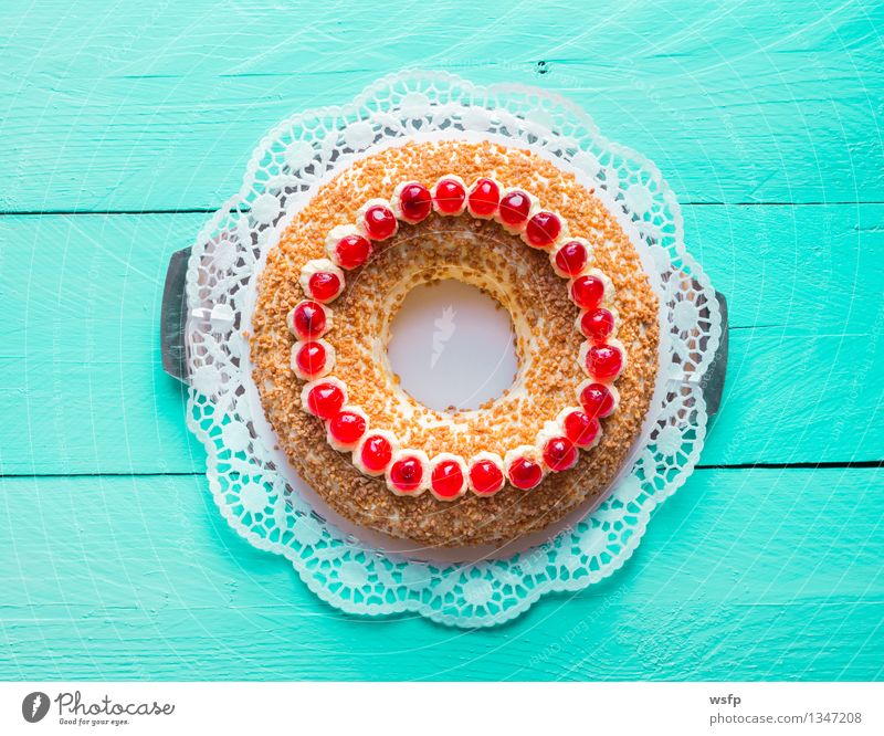 Frankfurter Kranz mit Kirschen auf türkisem Holz Kuchen Dessert Buttercremetorte ringförmig kranzförmig Schaumgebäck Sahne Torte Tortenspitze Backwaren Biskuit