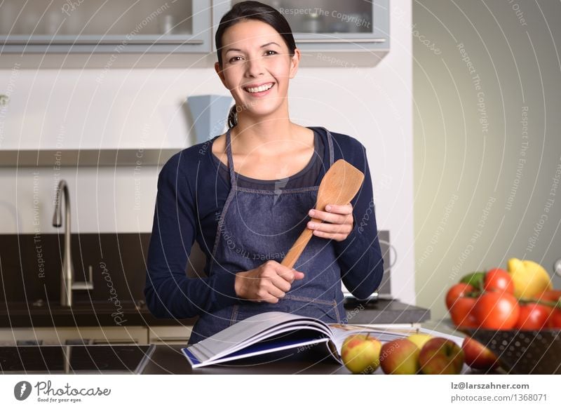 Frau, die Schöpflöffel beim Ablesen eines Kochbuchs hält Gemüse Frucht Ernährung Schalen & Schüsseln Glück Gesicht Küche Gastronomie Erwachsene 1 Mensch