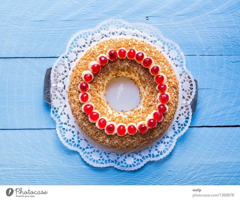 Frankfurter Kranz mit Kirschen auf blauem Holz Kuchen Dessert Buttercremetorte ringförmig kranzförmig Schaumgebäck Sahne Torte Tortenspitze Backwaren Biskuit