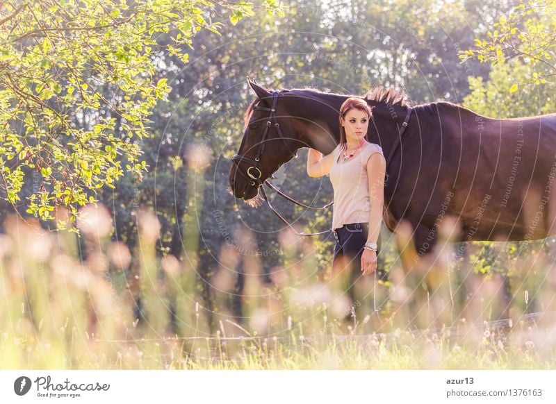 Schöne junge Reiterin Frau mit Pferd in der Natur. Liebe und Freundschaft zwischen Mensch und Tier. Portrait in der Landschaft beim Pferdestall von Reiterhof mit Reitschule oder Bauernhof mit Haustier für Hobby Reiten.