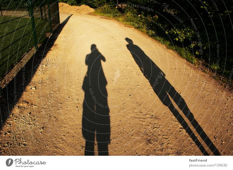 Die Geschichte der Ungleicheit einer Freundschaft Licht Zaun lang dunkel Silhouette Umrisslinie lang gezogen Am Rand Zusammensein wandern groß klein dünn Sommer