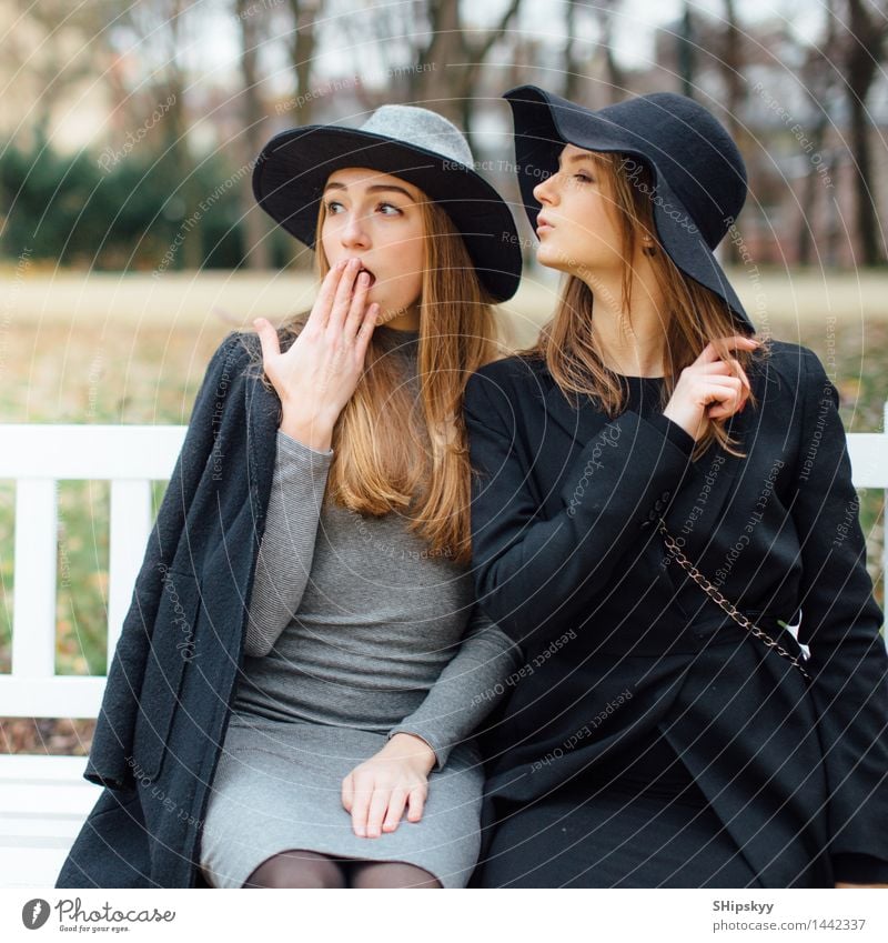 Zwei Mädchen, die auf Bank im Parkhintergrund sitzen Lifestyle kaufen Stil Design schön Schminke Winter Schnee Garten Nachtleben Veranstaltung Junge Frau