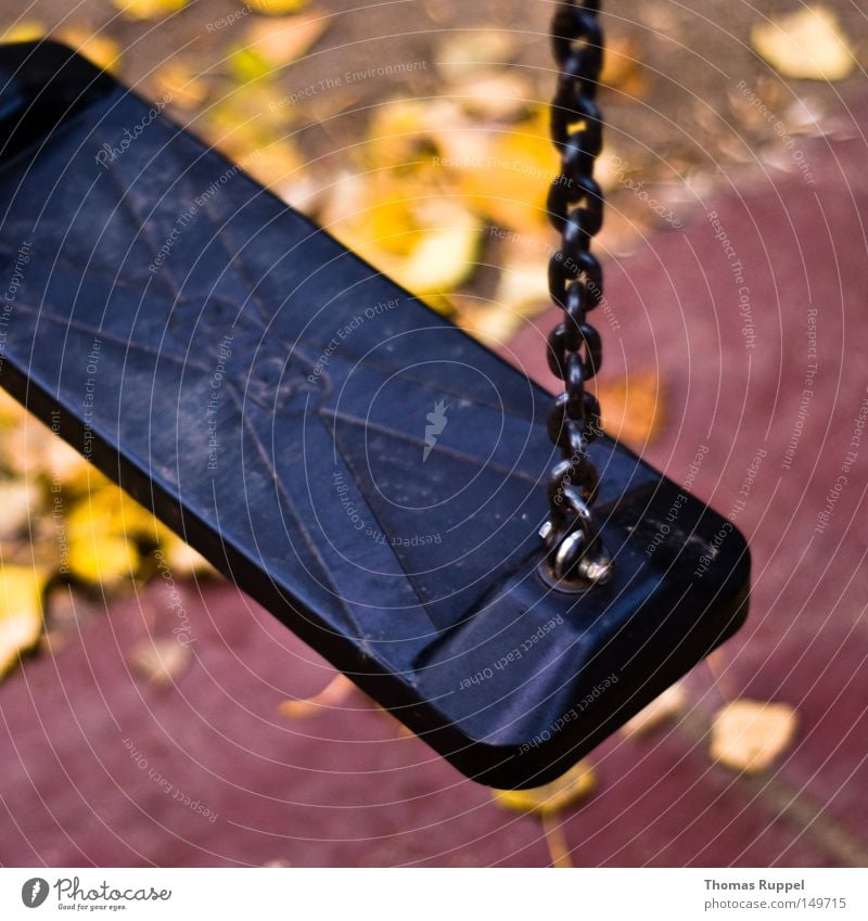 Stillstand auf dem Spielplatz Schaukel dunkel grau schwarz Menschenleer Kette Blatt Unschärfe gelb Herbst Spielzeug Kindheit Spielen Freude Außenaufnahme