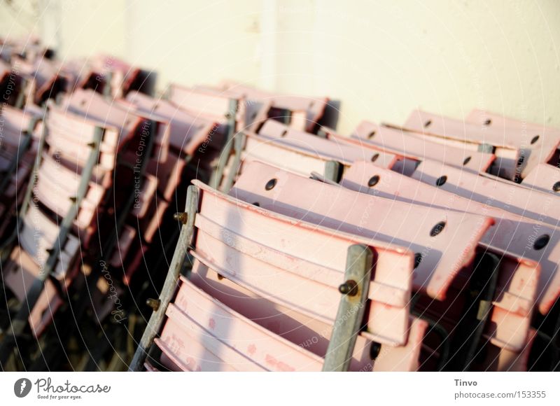 zusammengeklappte Klappstühle Klappstuhl Gartenstuhl rosa Rost angelehnt Sonne Terrasse Saisonende trist vergessen Café Treffpunkt Gastronomie ausgebleicht