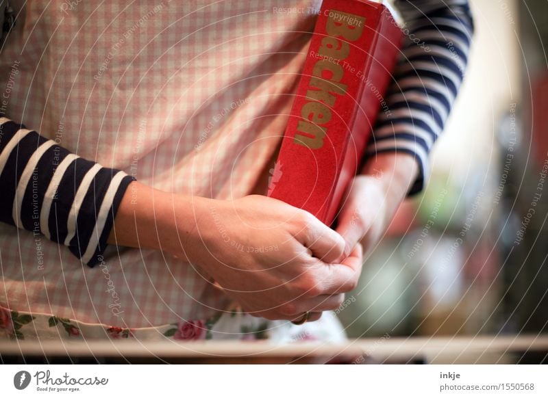 Mutti backt. Lifestyle Küche Frau Erwachsene Leben Körper Hand 1 Mensch Schürze Buch Backbuch Kochbuch Schriftzeichen festhalten Gefühle Vorfreude Optimismus