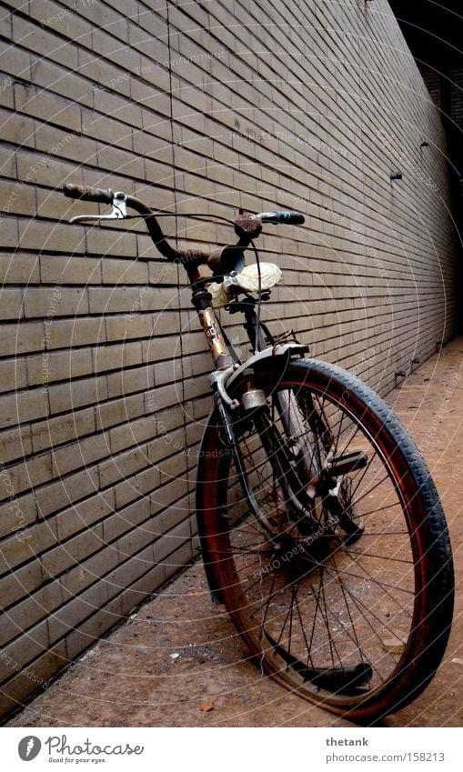 Ein altes Fahrrad mit platten Reifen lehnt an einer Klinkerwand in einer Fabrikhalle. ruhig Rost Backstein kaputt Einsamkeit Vergangenheit Vergänglichkeit