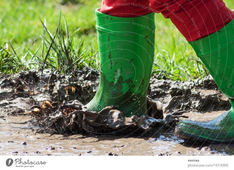 Grüne Gummistiefel platschen in matschige Pfütze Schlamm Matsch Spielen Kind Fuß Mensch Wasser Wassertropfen Wiese springen dreckig nass braun grün rot Freude