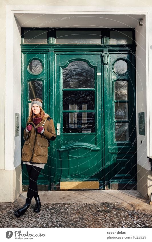 Junge Frau steht vor grüner Eingangstür Lifestyle Zufriedenheit Winter Mensch feminin Jugendliche 1 18-30 Jahre Erwachsene Stadt Hauptstadt Tür Jacke brünett