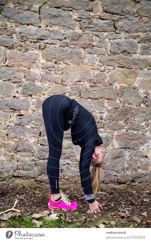 Frau, die ihren Körper vor der alten Mauer im Park ausstreckt. Lifestyle Wellness Sport Mensch Erwachsene Stein berühren Fitness sportlich Mobilität üben