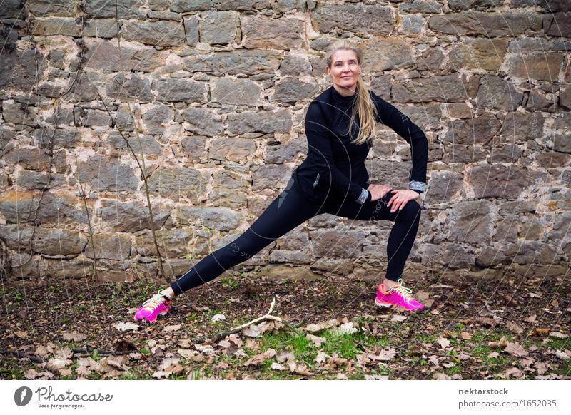 Frau, die ihren Körper vor der alten Mauer im Park ausstreckt. Lifestyle Glück Wellness Sport Mensch Erwachsene Stein Fitness Lächeln sportlich Freundlichkeit