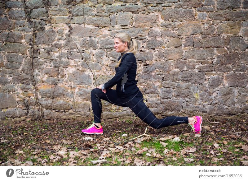 Frau, die ihren Körper vor der alten Mauer im Park ausstreckt. Lifestyle Glück Wellness Sport Mensch Erwachsene Stein Fitness Lächeln sportlich Freundlichkeit