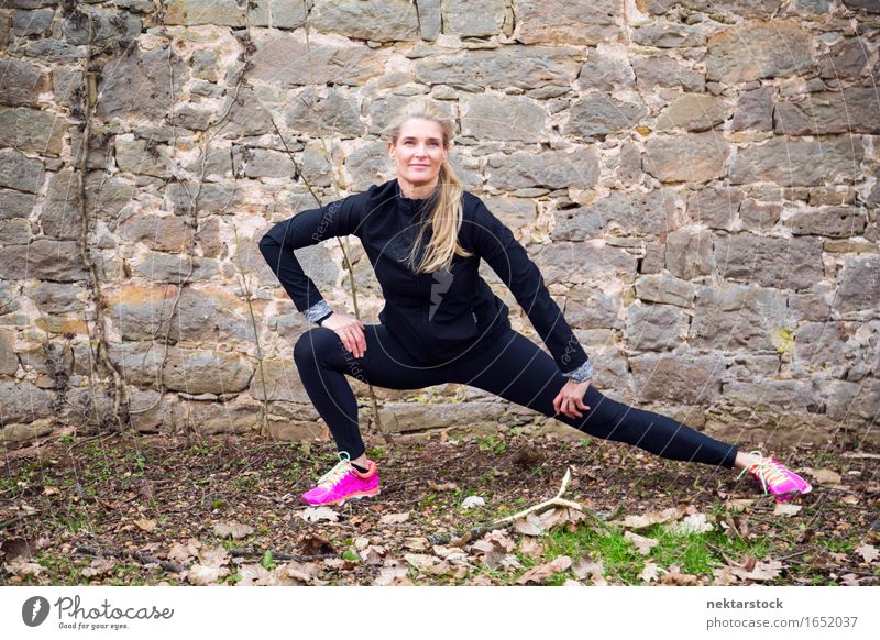 Frau, die ihren Körper vor der alten Mauer im Park ausstreckt. Lifestyle Glück Wellness Sport Mensch Erwachsene Stein Fitness Lächeln sportlich Freundlichkeit