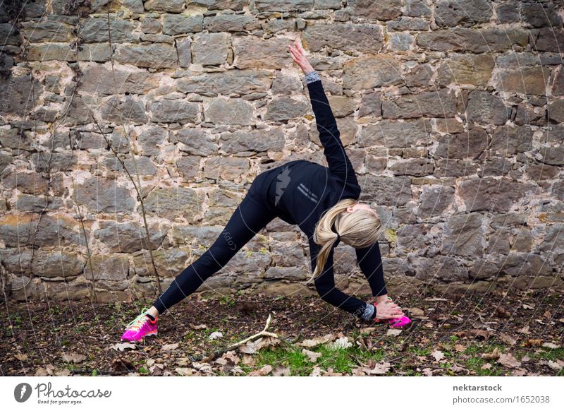 Frau, die ihren Körper vor der alten Mauer im Park ausstreckt. Lifestyle Glück Wellness Sport Mensch Erwachsene Stein Fitness Lächeln sportlich Freundlichkeit