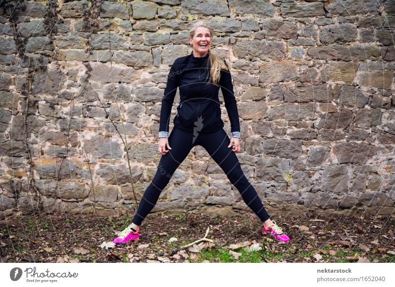 Frau, die ihren Körper vor der alten Mauer im Park ausstreckt. Lifestyle Glück Wellness Sport Mensch Erwachsene Stein Fitness Lächeln sportlich Freundlichkeit