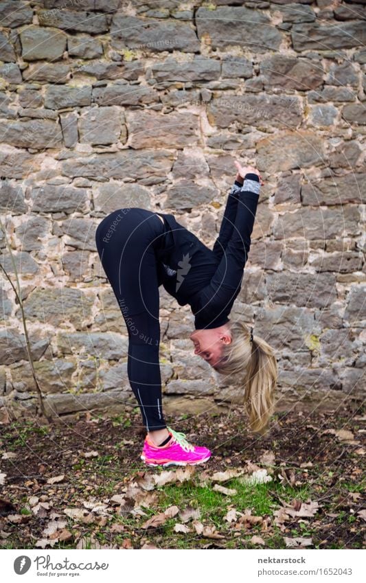 Frau, die ihren Körper vor der alten Mauer im Park ausstreckt. Lifestyle Glück Wellness Sport Mensch Erwachsene Stein Fitness Lächeln sportlich Freundlichkeit