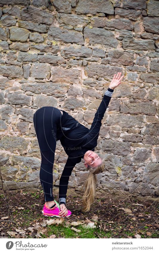 Frau, die ihren Körper vor der alten Mauer im Park ausstreckt. Lifestyle Glück Wellness Sport Mensch Erwachsene Stein Fitness Lächeln sportlich Freundlichkeit