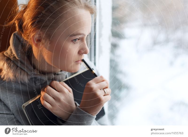 Junges Mädchen träumt am Fenster mit Notizbuch und Stift Gesicht Winter Wohnung Schüler Student Büro Business Mensch Junge Frau Jugendliche Erwachsene 1