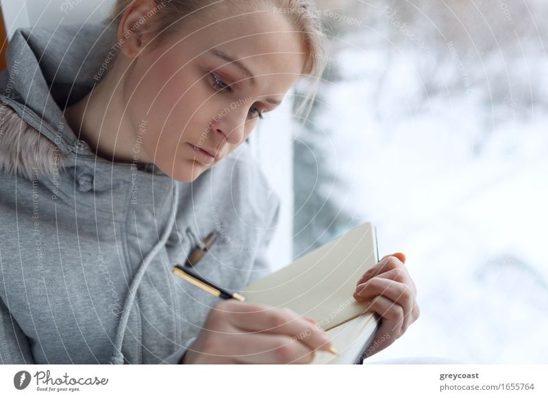 Junges Mädchen schreibt in ihr Tagebuch, während sie an einem großen Fenster sitzt. Windstille lesen Winter Bildung Schüler Student Büro Junge Frau Jugendliche