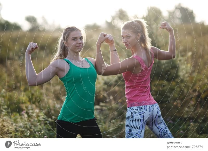 Zwei sportliche junge Mädchen im Stehen im Freien flexing ihre Armmuskeln während eines Trainings im Garten Sommer Sport Junge Frau Jugendliche Erwachsene Arme