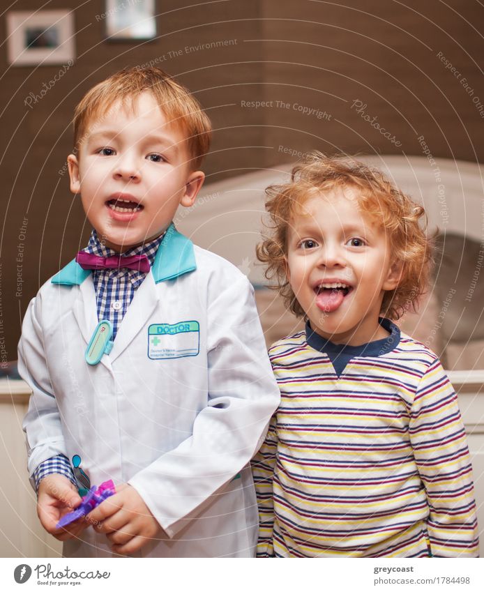 Zwei kleine Jungen als Arzt und Patient. Arzt ist im Laborkittel, ein anderes Kind zeigt die Zunge beim Lächeln Gesundheitswesen Spielen Krankenhaus blond