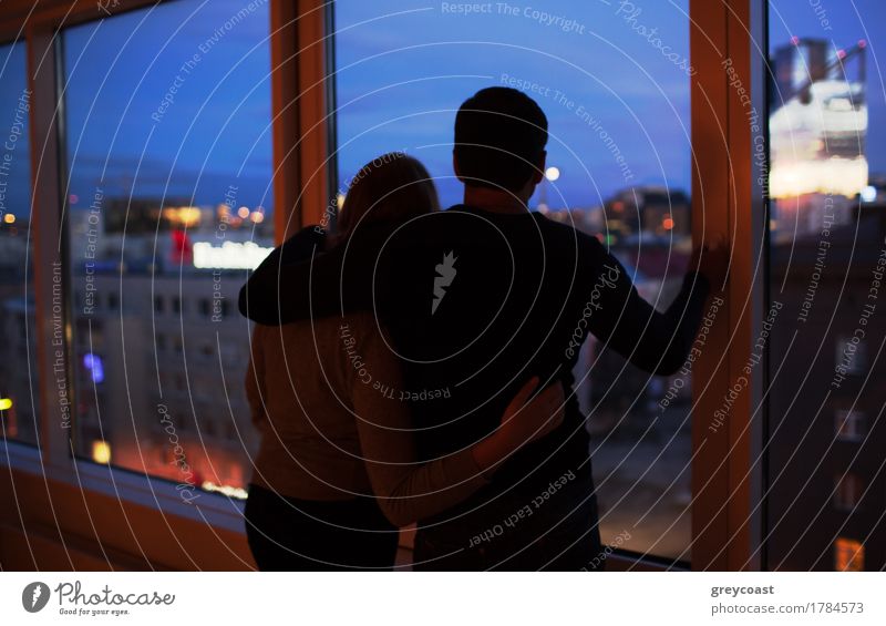 Zurück Schuss von jungen liebenden Paar durch das Fenster in der Nacht. Sie umarmen sich und genießen die Aussicht auf die Stadt. Romantische Momente Windstille