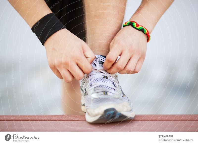 Nahaufnahme eines Mannes beim Binden von Laufschuhen mit Fuß auf der Bank. Bereitmachen vor dem Joggen. Gehen in für Sport, gesunden Lebensstil Lifestyle