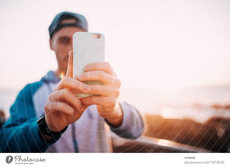 Junger erwachsener Mann, der Foto mit dem intelligenten Telefon im Freien macht Lifestyle Strand Meer PDA Fotokamera Technik & Technologie Mensch Junger Mann