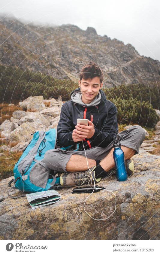 Junge, der auf einem Felsen stillsteht und einen Handy auflädt Flasche Lifestyle Freizeit & Hobby Ferien & Urlaub & Reisen Tourismus Ausflug Abenteuer Freiheit