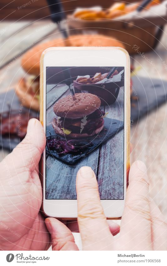 Hand mit Smartphone Handy, Foto von Burger auf Tisch Lebensmittel Fleisch Brot Brötchen Cheeseburger Speck soziale medien teilen Internet Telefon PDA Holz