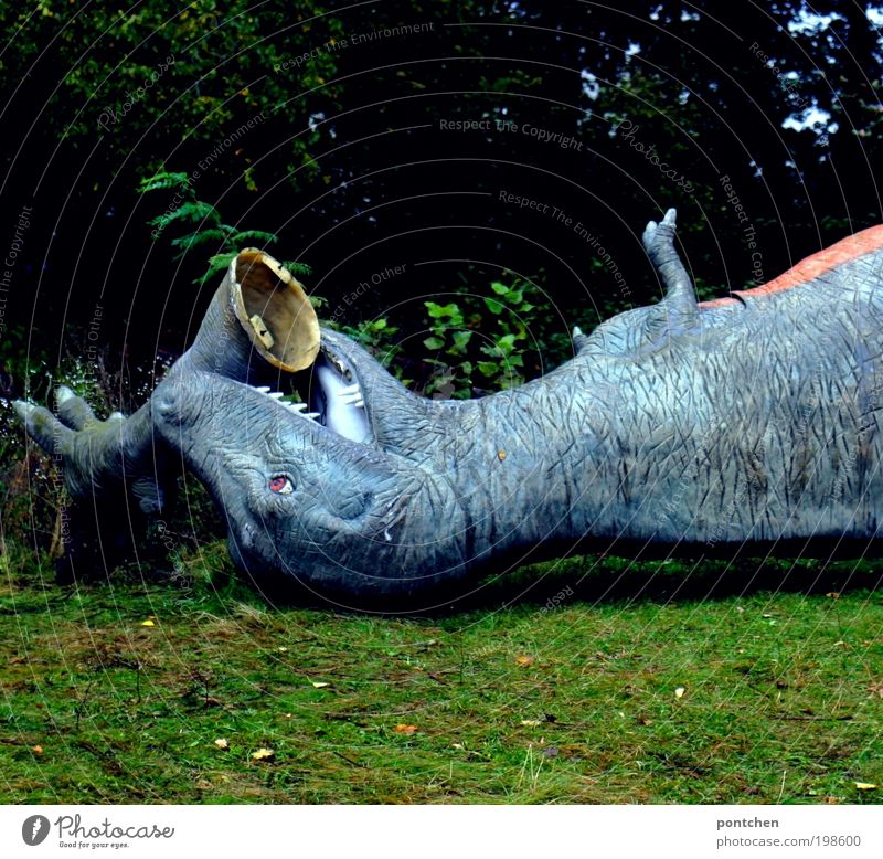 Zerstörte Figur eines tyrannosaurus rex liegt  im Gras und hat eigenes Bein im Mund. Verlassener Freizeitpark Freizeit & Hobby Vergnügungspark