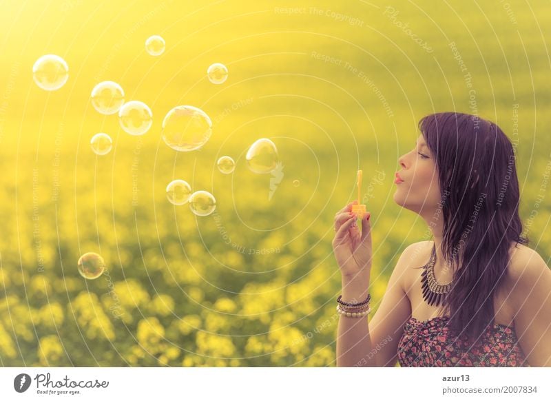 Schöne junge Frau mit Seifenblasen im Sommer auf gelber Wiese aus Raps bis zum Horizont. Hübsches Mädchen mit Lebensfreude geniesst die Sonnenschein Pause und das Leben. Erholung und Energie tanken vom Zeit Stress in der Umwelt und Natur Idylle.