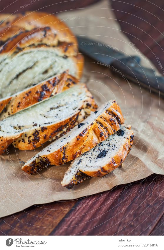 Geschnittene Rolle mit Mohn und Rosinen Brot Brötchen Dessert Essen Frühstück Messer Tisch Papier Holz frisch oben braun schwarz Korn Mahlzeit Scheibe süß