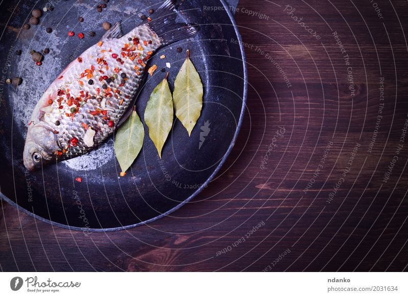 Karpfen mit Gewürzen in einer schwarzen Gusseisenpfanne Lebensmittel Fisch Kräuter & Gewürze Ernährung Pfanne Tisch Küche Holz Diät Essen frisch oben braun grün