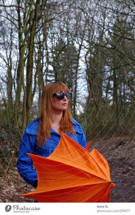 rothaariger hübscher Teenager, langhaarig mit schwarzer Sonnenbrille, blauer Jacke, orangefarbenem Schirm im Wald Frau besonnen bedächtig schön Regenschirm